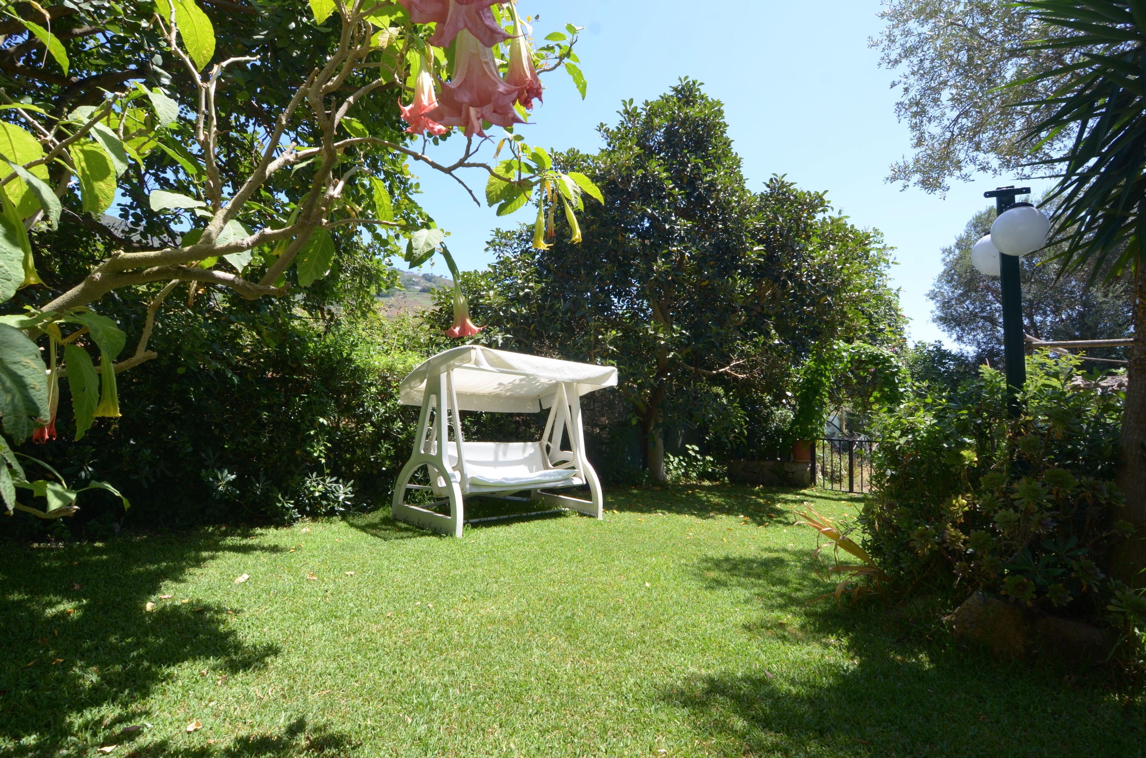 A garden with a white swing set, lush greenery, and a lamp post.