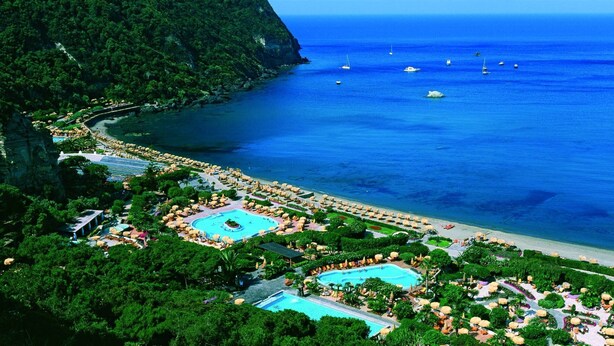 A resort with multiple swimming pools, a beach, and a mountainous backdrop.
