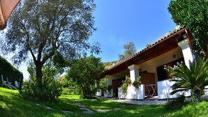 A house with a covered porch, surrounded by lush greenery and a clear blue sky.
