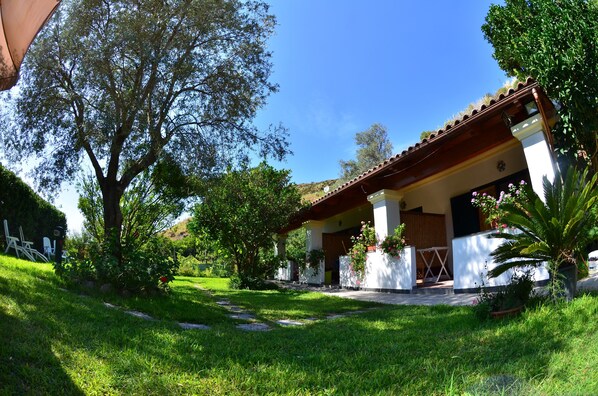 A house with a covered porch, surrounded by lush greenery and a clear blue sky.