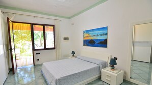 A bedroom with a bed, bedside tables, a painting, and a door leading to a balcony.