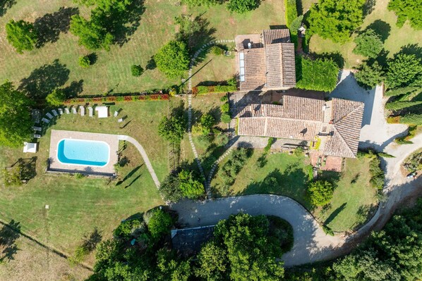 An aerial view of a property with a swimming pool, a patio area with seating, and a large building with a tiled roof.