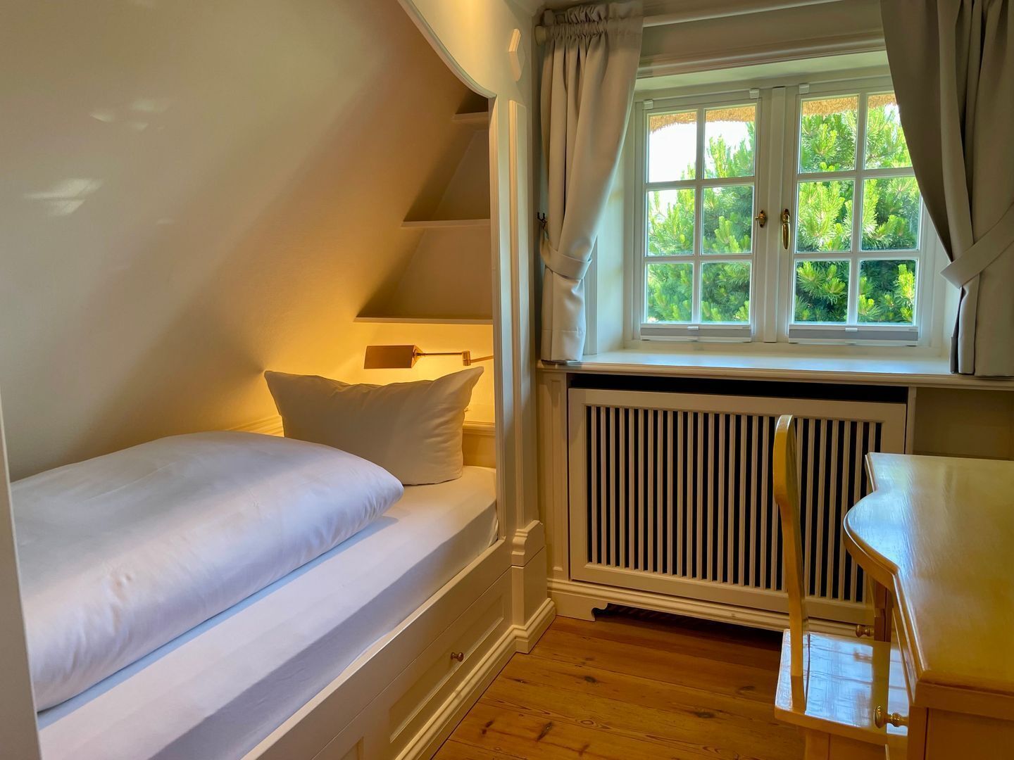 A bedroom with a single bed, a window with curtains, a radiator, and a chair.