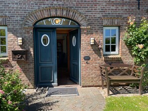 A traditional brick building with a large arched entrance, a mailbox labeled "POSTKASTEN", and a wooden bench outside. - Landhaus Sylt Glück - Holiday home Sylt Glück Morsum, 135sqm for up to 5 people (Sylt-Ost)