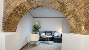 A cozy living room with a brick archway, a sofa set, a white armchair, and a small table with decorative items. - ChezmoiHomes Realejo Boutique Terrace (Granada)