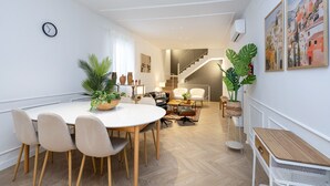 A modern living room with a dining area, featuring a white table, chairs, and a staircase leading to an upper floor. - ChezmoiHomes Realejo Boutique Terrace (Granada)