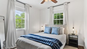 A bedroom with a bed, two bedside tables, a ceiling fan, and windows with curtains.