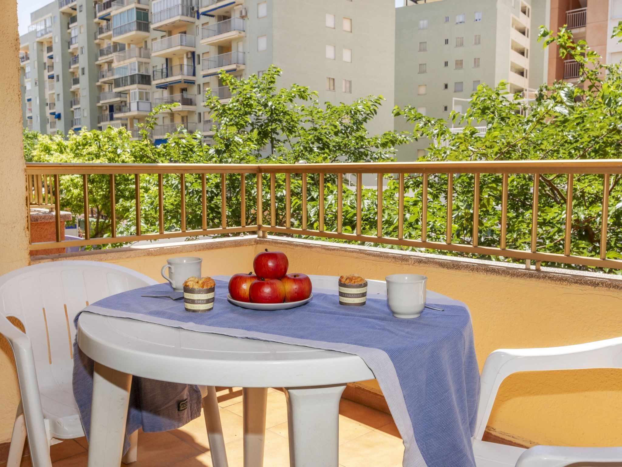 Un balcón con una mesa dispuesta para el desayuno, incluyendo manzanas, pasteles y una taza de café.