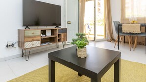 Una sala de estar moderna con un televisor de pantalla plana, un mueble de entretenimiento de madera, una mesa de centro con una planta, y un comedor con mesa y sillas.