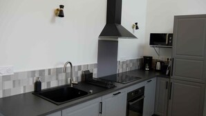 Una cocina moderna con gabinetes grises, un lavamanos negro, una campana extractora de acero inoxidable, un microondas y un horno empotrado.