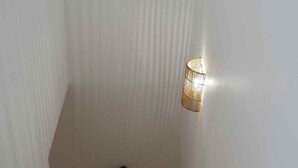 Una escalera estrecha con piso de madera, paredes blancas y una única lámpara.
