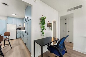 Een moderne keuken met lichtblauwe kastjes, een witte koelkast en een eethoek met een zwarte tafel en blauwe stoelen.