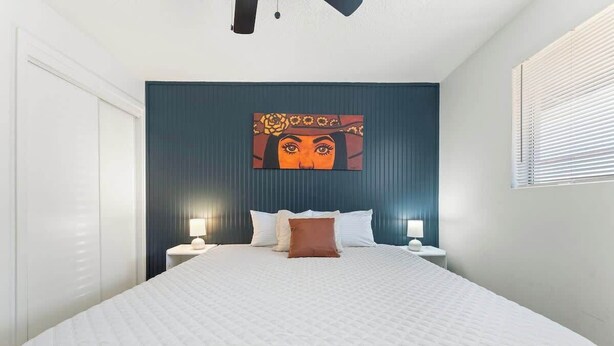 A bedroom with a bed, two bedside tables, a wall-mounted artwork, and a window with blinds.