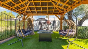 A covered outdoor seating area with two swing chairs and a table.