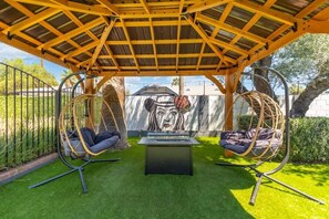 A covered outdoor seating area with two swing chairs and a table.
