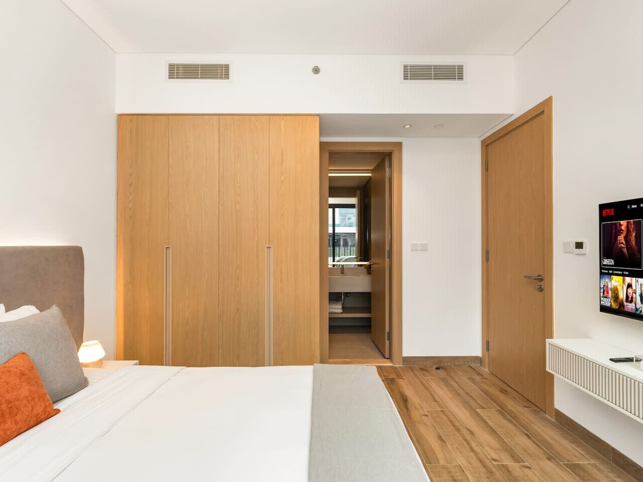 A modern bedroom with a large bed, wooden wardrobe, and a TV on the wall.