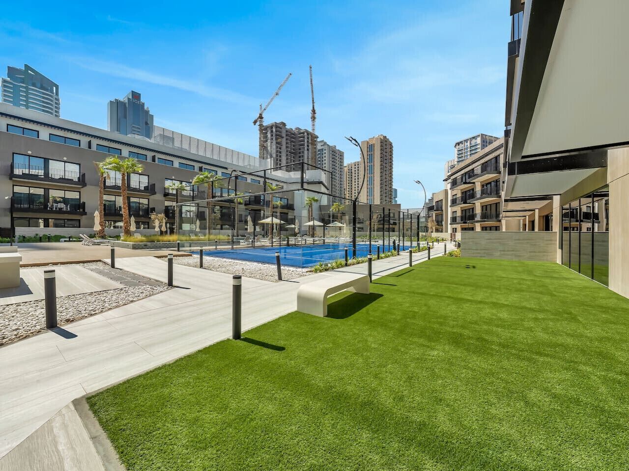 Un área de piscina exterior moderna con una piscina azul, rodeada por un césped cuidado y senderos de hormigón.