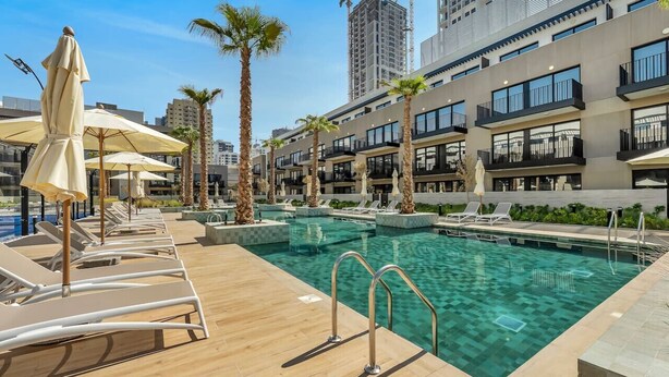 A rooftop pool area with sun loungers, umbrellas, and a clear view of the city skyline. - Brand New Luxury 2Bedroom in JVC with 5* Amenities (Dubai)