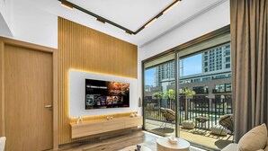 A modern living room with a large TV, wooden panel wall, and a balcony with outdoor furniture. - Brand New Luxury 2Bedroom in JVC with 5* Amenities (Dubai)
