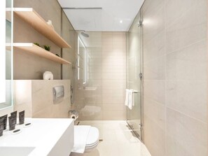 Ein modernes Badezimmer mit einer Duschkabine aus Glas, einem weißen Waschbecken und beigen Fliesen.