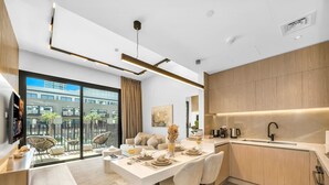 A modern kitchen with a dining area, large windows, and a view of buildings. - Brand New Luxury 2Bedroom in JVC with 5* Amenities (Dubai)