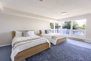 A bedroom with two beds, a large window with a view of trees, and a blue carpet. - Soar Above the Sea at Eagle’s Perch Oceanfront Retreat (Nanoose Bay)