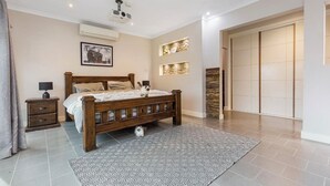 Un dormitorio con cama de madera, una mesita de noche, una alfombra, aire acondicionado instalado en la pared y un armario con puerta corredera.