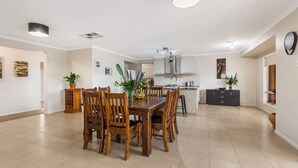 Un amplio comedor con una mesa y sillas de madera, una cocina al fondo y un reloj en la pared.