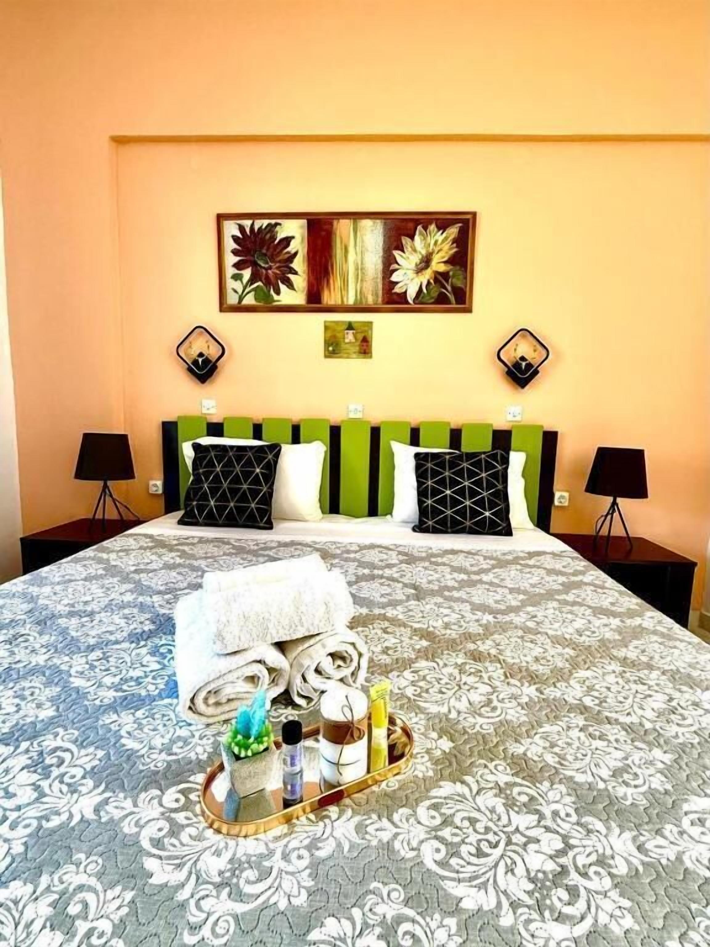 A hotel room with a bed, green and black pillows, a tray with toiletries, and two wall-mounted lamps.