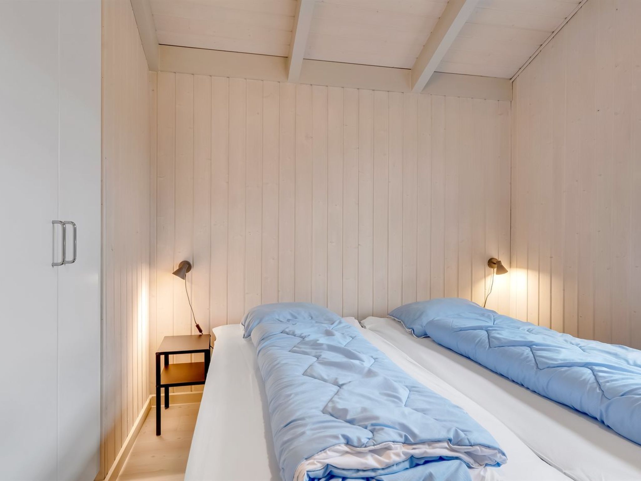 Une chambre avec deux lits, des murs en bois et des lampes de chevet.