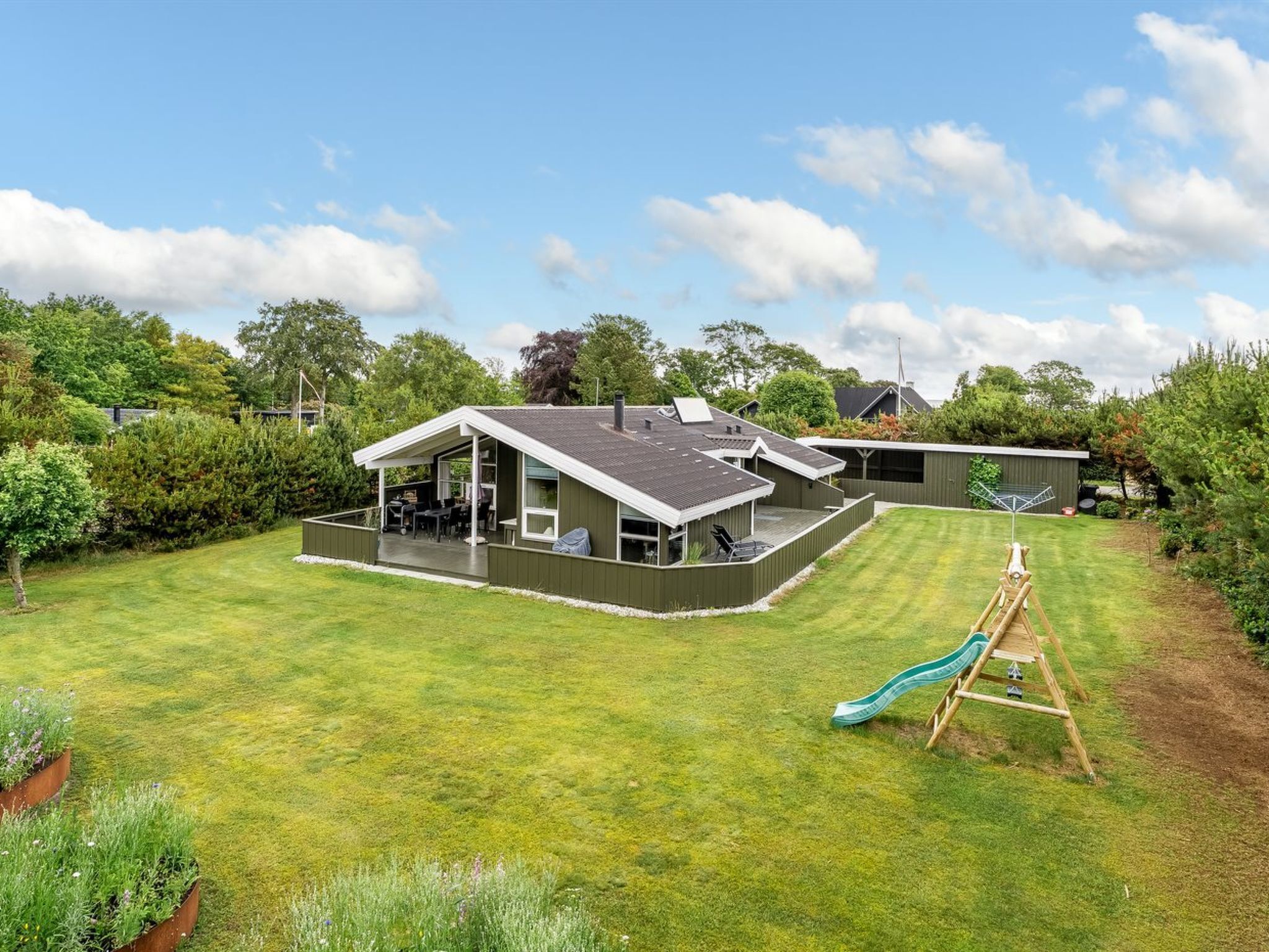 A modern house with a large backyard, a covered patio, and a slide.