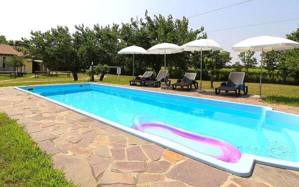 Ein rechteckiger Pool mit Steinbordstein, umgeben von Liegestühlen und Sonnenschirmen.