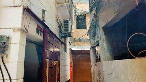 Une ruelle étroite, avec une porte en bois fermée au bout, bordée d’immeubles dont les câbles électriques sont apparents et surmontée d’une structure en béton.