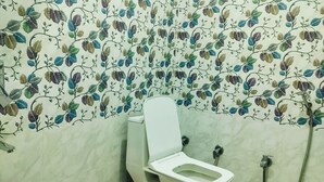 Une salle de bain avec des toilettes, une douche et un seau rouge.