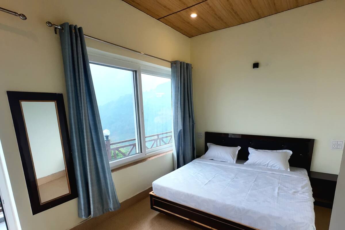 A bedroom with a bed, a ceiling fan, a window with curtains, and a view of the outdoors.