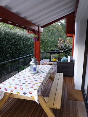 A covered outdoor patio with a table set for dining, a bench, and a small table with drinks.