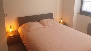 Makuuhuone, jossa on sänky, yöpöytävalaisimet, geometrisesti muotoiltu riippuvalaisin ja seinätaidetta.