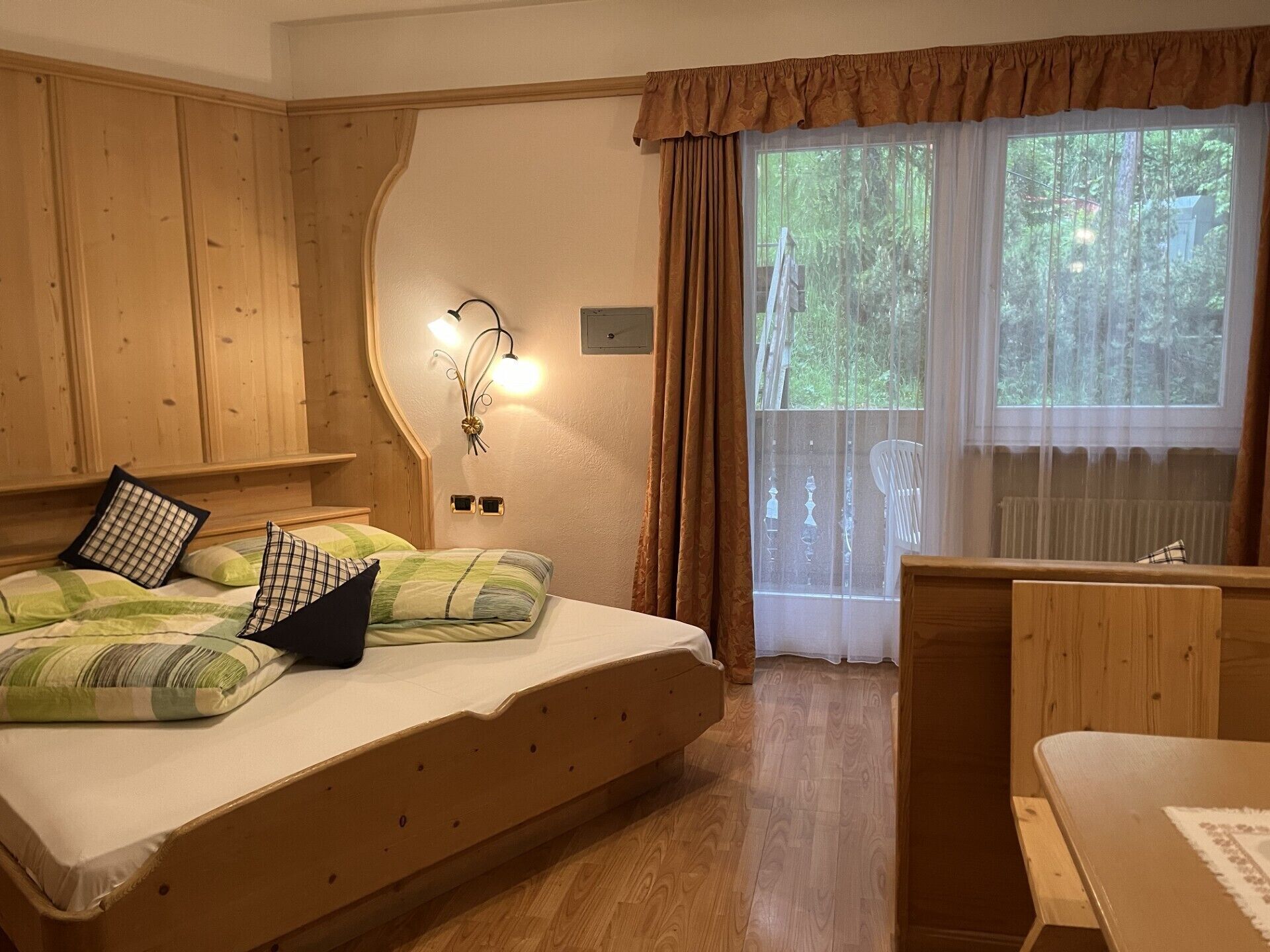 A wooden room with a bed, a desk, and a window with curtains.