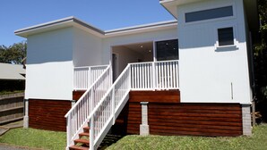 A two-story house with a white exterior, a wooden deck, and a staircase leading to the upper floor. - 5 mins walk to Beach - Modern Beachy Escape. Netflix, Full Kitchen, Comfy Beds! (Terrigal)