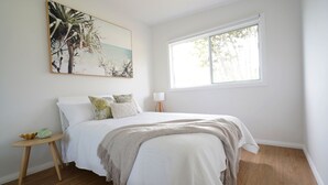 A bedroom with a bed, a window, a bedside table, and a wall-mounted painting. - 5 mins walk to Beach - Modern Beachy Escape. Netflix, Full Kitchen, Comfy Beds! (Terrigal)