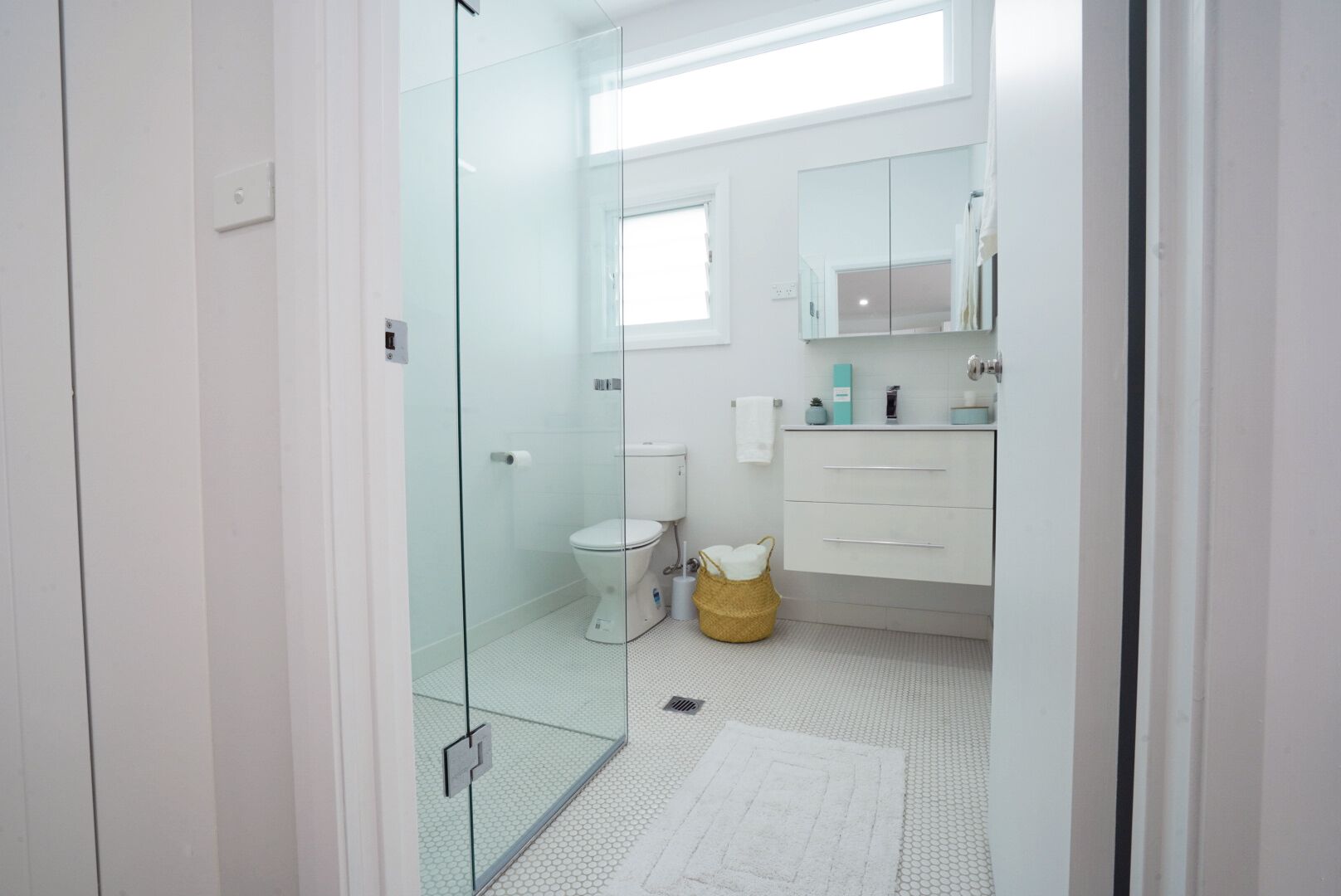 Un baño moderno con cabina de ducha de vidrio, inodoro, lavamanos con espejo y un ventanal.