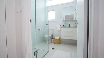 Un baño moderno con cabina de ducha de vidrio, inodoro, lavamanos con espejo y un ventanal.