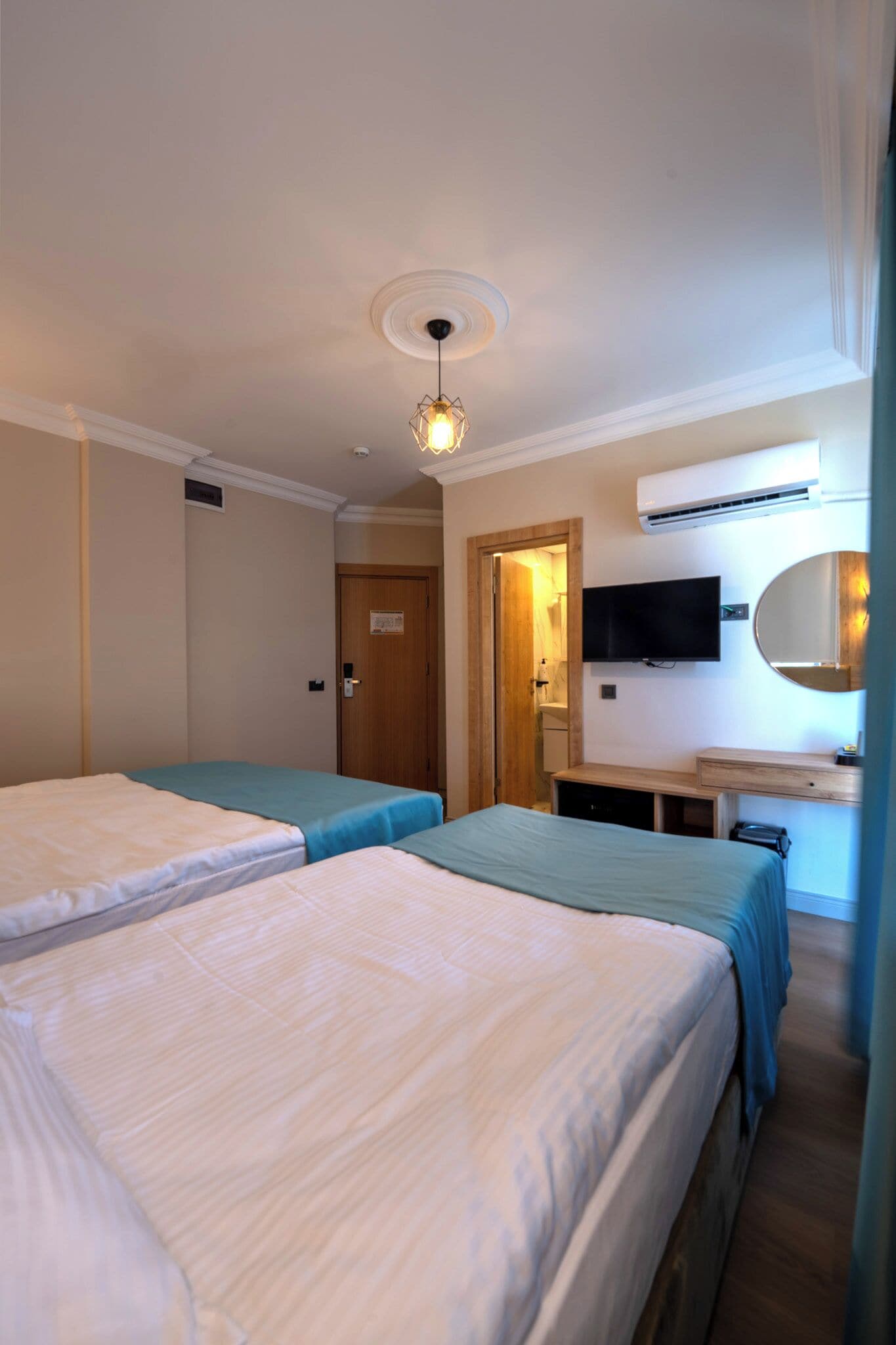 Habitación de hotel con dos camas, televisor, espejo y aire acondicionado.