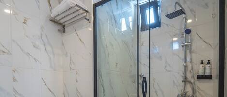 A bathroom with a glass-enclosed shower, a toilet, and a marble-tiled floor.