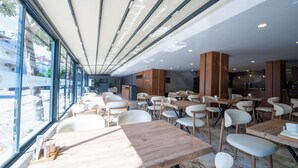 Un restaurante moderno con amplios ventanales, mesas de madera y sillas blancas.