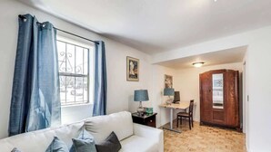 Una sala de estar con un sofá blanco, piso de madera, un escritorio con una computadora y una puerta de madera.