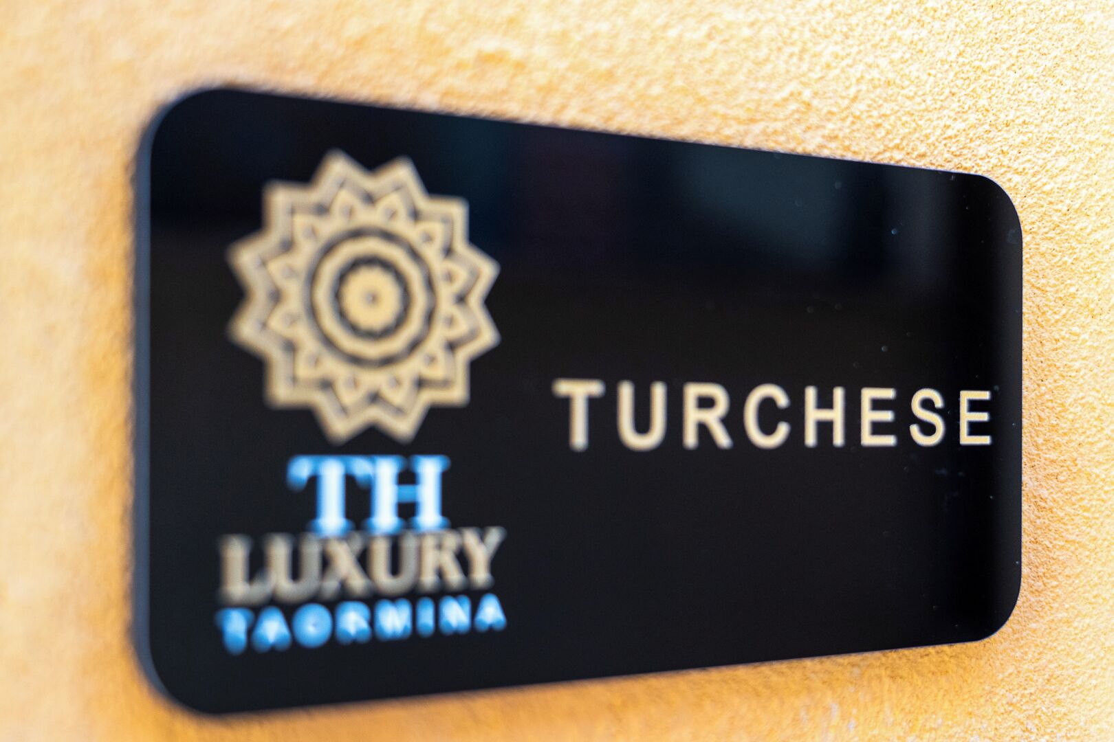 A black sign with the text "TH LUXURY" and "TURCHSE" on a textured wall.