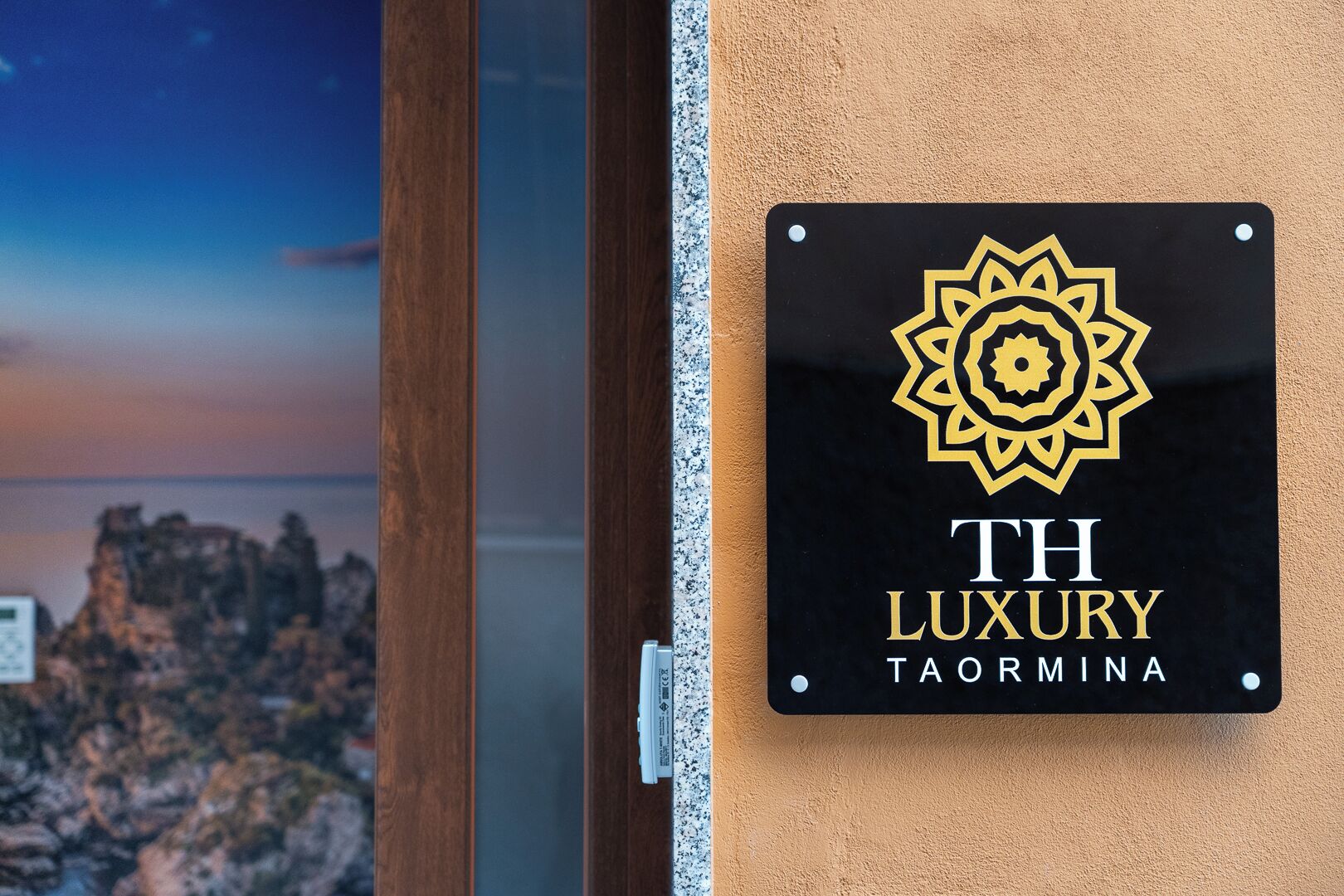 Une enseigne avec un logo et l’inscription « TH LUXURY TAORMINA » sur un mur.