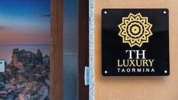 Un senyal amb un logotip i el text 'TH LUXURY TAORMINA' a la paret.