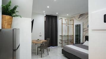 Una habitación de hotel moderna con una cama, una mesa de comedor con sillas, un refrigerador y una planta.